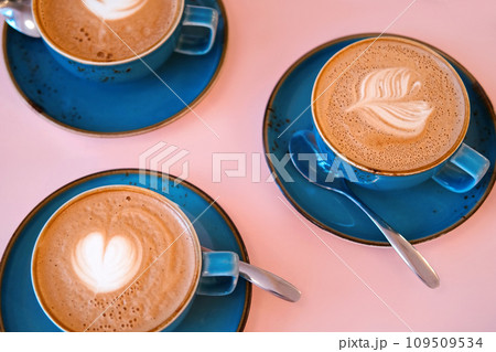 Cup of Cappuccino with Art Milk Foam Top View. Latte with Steel Spoon. Hot Coffee in a Blue Ceramic Mug With Saucer on a Pink Table. Modern Glamour Coffee Shop, Cafeteria. Thick Froth. No People. 4K 109509534