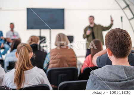 Engaged audience listening to a presenter at an informal outdoor event, focus on foreground listeners.  109511830