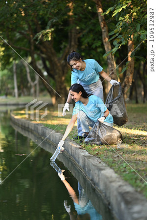 Happy young volunteer women collecting trash in the public park. Environmental protection and charity concept 109512987