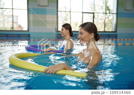Two young women training with noodles at swimming pool Two young women training with noodles at swimming pool 109514360