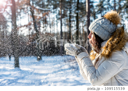 Happy woman dressed white sweater and hat blowing snow 109515539