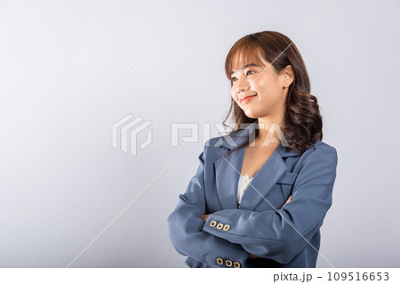 Confident Asian woman with a radiant smile, standing with crossed arms in a studio shot on a white background. Copy space available for your message. 109516653