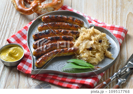 Six fried Nuremberg sausages with sauerkraut on a heart-shaped pewter plate, served with a pretzel Six fried Nuremberg sausages with sauerkraut on a heart-shaped pewter plate, served with a pretzel 109517768