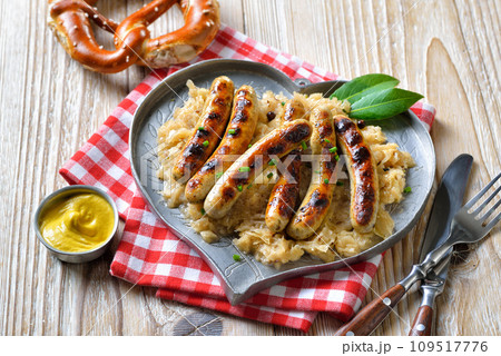 Six fried Nuremberg sausages with sauerkraut on a heart-shaped pewter plate, served with a pretzel 109517776