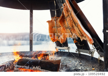 Smoked salmon fish fillet pinned on wooden plank board grilled on open fire pit outdoors. Traditional north Europe finnish Lapland seafood dish. Healthy natural nutrition on food fest party market Smoked salmon fish fillet pinned on wooden plank board grilled on open fire pit outdoors. Traditional north Europe finnish Lapland seafood dish. Healthy natural nutrition on food fest party market 109520492
