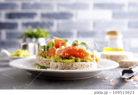 open sandwiches with rye bread, avocado, smoked salmon on a white plate 109523623