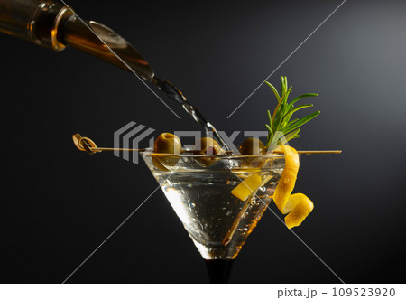 Classic dry martini cocktail with green olives, lemon peel, and rosemary on a black background. 109523920