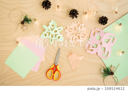 Colorful paper snowflakes cutouts, on a wooden background. Cutting snowflakes from colored paper. Snowflake winter background. Simple winter kids crafts idea. 109524612