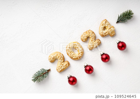 Cookies in the form of numbers 2024 by diagonal on the white background decorated with pine twig and christmas toys. 109524645
