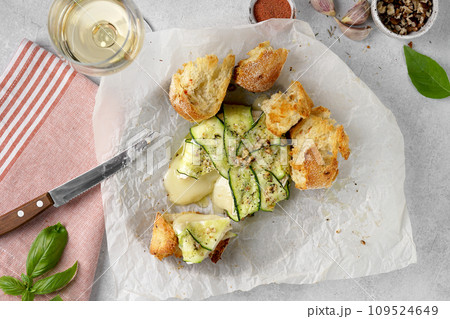Baked Brie camembert cheese with zucchini with nuts, herbs and olive oil. Served with wine and bread 109524649