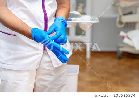 Close up of a female doctor putting a blue latex gloves on a clinic background. 109525574