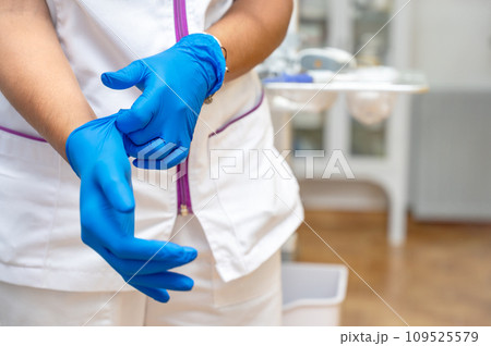 Close up of a female doctor putting a blue latex gloves on a clinic background. 109525579