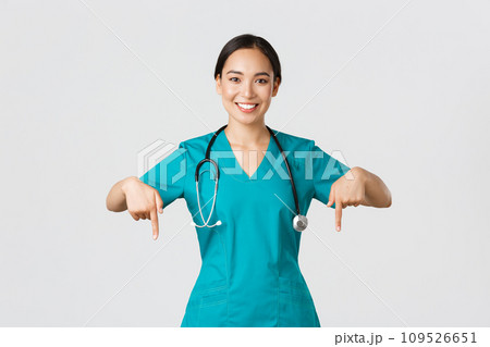 Covid-19, healthcare workers, pandemic concept. Smiling pleasant asian female doctor, therapist or physician in scrubs with stethoscope, pointing fingers down, show clinic banner Covid-19, healthcare workers, pandemic concept. Smiling pleasant asian female doctor, therapist or physician in scrubs with stethoscope, pointing fingers down, show clinic banner 109526651