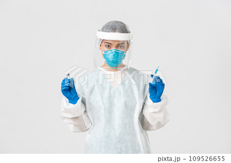 Covid-19, coronavirus disease, healthcare workers concept. Confident asian female doctor, physician in personal protective equipment and respirator, ready make ingection, holding syringe with vaccine 109526655