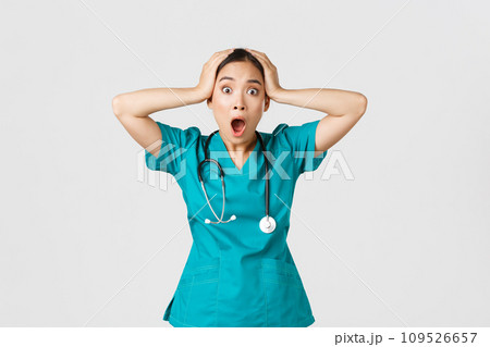 Covid-19, healthcare workers and preventing virus concept. Shocked and anxious asian female doctor in panic, grab head and screaming alarmed, have big problem, got in trouble, white background Covid-19, healthcare workers and preventing virus concept. Shocked and anxious asian female doctor in panic, grab head and screaming alarmed, have big problem, got in trouble, white background 109526657
