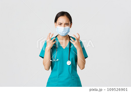 Covid-19, coronavirus disease, healthcare workers concept. Angry and pissed-off asian female doctor, physician in medical mask and scrubs, clench fists outraged, looking furious, white background 109526901
