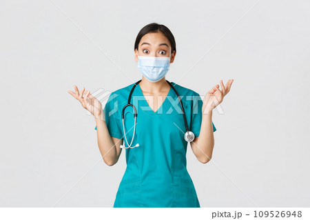 Covid-19, coronavirus disease, healthcare workers concept. Surprised and amazed asian female nurse, physician in medical mask and scrubs raising hands up excited, hear amazing news, white background 109526948
