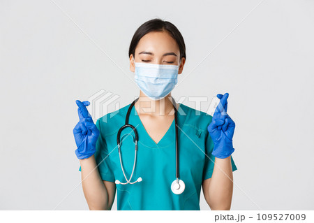 Covid-19, coronavirus disease, healthcare workers concept. Close-up of hopeful asian female doctor, physician in medical mask and rubber gloves, making wish, cross fingers good luck Covid-19, coronavirus disease, healthcare workers concept. Close-up of hopeful asian female doctor, physician in medical mask and rubber gloves, making wish, cross fingers good luck 109527009