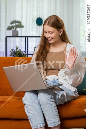 Teenager red hair girl sitting on home couch, making video conference call with friends or family 109527097