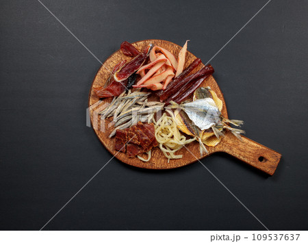 Snack board with dried and salted fish and squid. Top view on black background, copy space. fish plate Snack board with dried and salted fish and squid. Top view on black background, copy space. fish plate 109537637