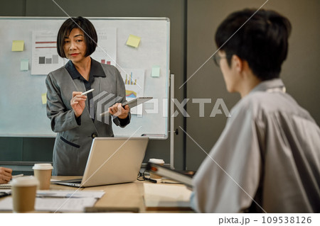 Senior female business team leader paying attention to younger employee expressing opinion in meeting. 109538126