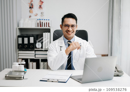 Physician doctor sit on table in hospital. Attractive therapist male practitioner pharmacist smile and use tablet and laptop. after success work from treatment 109538276