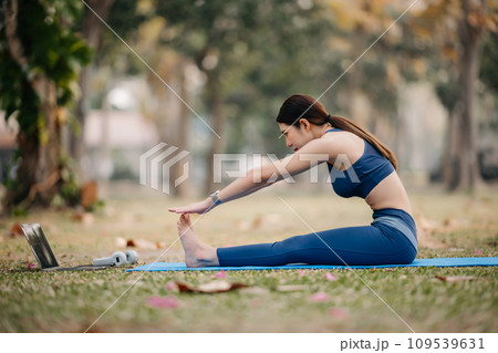 Portrait of young woman with closed eyes sitting in lotus position on yoga mat in the garden. sun light Portrait of young woman with closed eyes sitting in lotus position on yoga mat in the garden. sun light 109539631