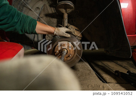 Using a wrench, a man unscrews the bolts on the car block. The driver is repairing the car in the garage. Taking care of your car and timely repairs and replacement of spare parts. 109541052