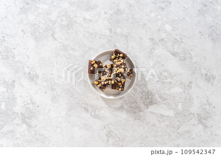 Flat lay. Homemade chocolate hazelnut fudge square pieces on a white plate. Flat lay. Homemade chocolate hazelnut fudge square pieces on a white plate. 109542347