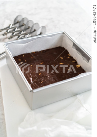 Freshly made homemade chocolate macadamia fudge in a square baking pan lined with parchment paper. 109542471