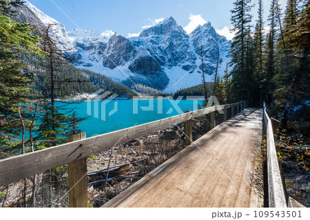 Moraine lake in autumn sunny day morning. Snow-capped Valley of the Ten Peaks. Lakeshore trail wooden bridge. Banff National Park, Canadian Rockies. Alberta, Canada. Moraine lake in autumn sunny day morning. Snow-capped Valley of the Ten Peaks. Lakeshore trail wooden bridge. Banff National Park, Canadian Rockies. Alberta, Canada. 109543501