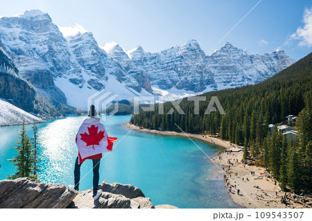 Tourist draped in Canadian flag looking beautiful scenery of Moraine lake. Banff National Park. Canadian Rockies. Alberta, Canada. Tourist draped in Canadian flag looking beautiful scenery of Moraine lake. Banff National Park. Canadian Rockies. Alberta, Canada. 109543507