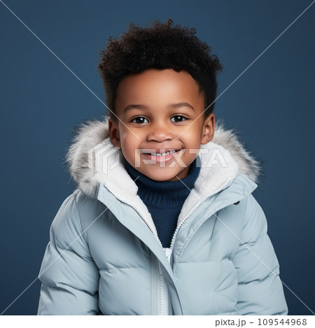 Little african boy in a blue winter coat. Studio portrait of a small boy in a winter jacket smiling on a blue background looking at the camera. Happy black child wearing warm winter clothes. 109544968