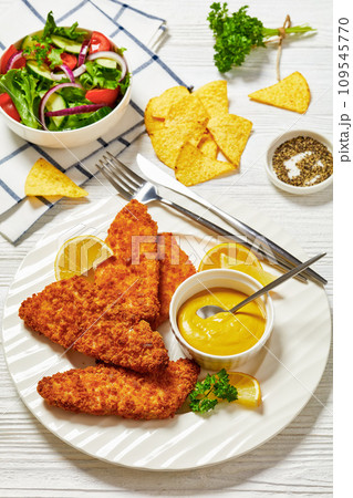 breaded fish fillet on plate with salad in bowl 109545770