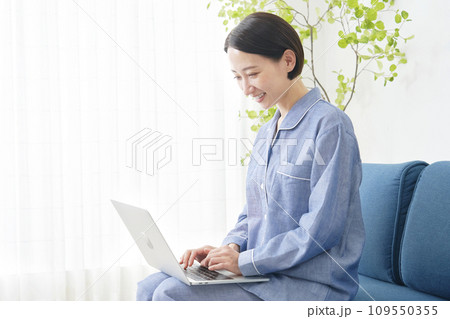 自宅でパジャマを着てノートパソコンを使う中年女性 自宅でパジャマを着てノートパソコンを使う中年女性 109550355