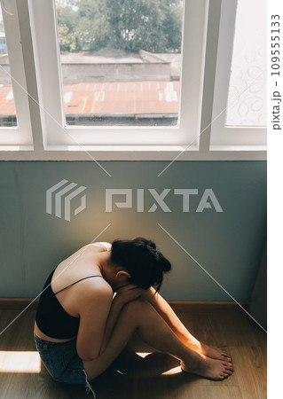 Thoughtful girl sitting on sill embracing knees looking at window, sad depressed teenager spending time alone at home, young upset pensive woman feeling lonely or frustrated thinking about problems Thoughtful girl sitting on sill embracing knees looking at window, sad depressed teenager spending time alone at home, young upset pensive woman feeling lonely or frustrated thinking about problems 109555133