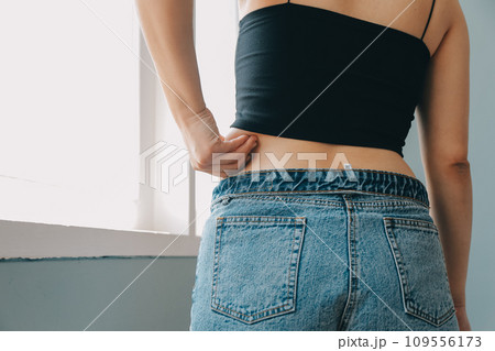 Close up of a belly with scar from c-section and abdominal fat. Women's health. A woman dressed up in sportswear demonstrating her imperfect body after a childbirth with nursery on the background. Close up of a belly with scar from c-section and abdominal fat. Women's health. A woman dressed up in sportswear demonstrating her imperfect body after a childbirth with nursery on the background. 109556173