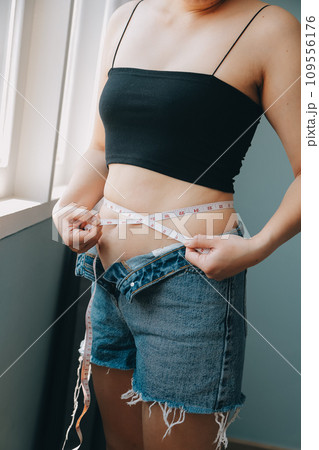 Close up of a belly with scar from c-section and abdominal fat. Women's health. A woman dressed up in sportswear demonstrating her imperfect body after a childbirth with nursery on the background. 109556176