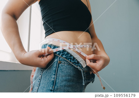 Close up of a belly with scar from c-section and abdominal fat. Women's health. A woman dressed up in sportswear demonstrating her imperfect body after a childbirth with nursery on the background. Close up of a belly with scar from c-section and abdominal fat. Women's health. A woman dressed up in sportswear demonstrating her imperfect body after a childbirth with nursery on the background. 109556179