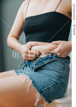 Close up of a belly with scar from c-section and abdominal fat. Women's health. A woman dressed up in sportswear demonstrating her imperfect body after a childbirth with nursery on the background. 109556187