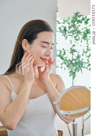 顔をマッサージして肌のお手入れをする30代女性 109559375