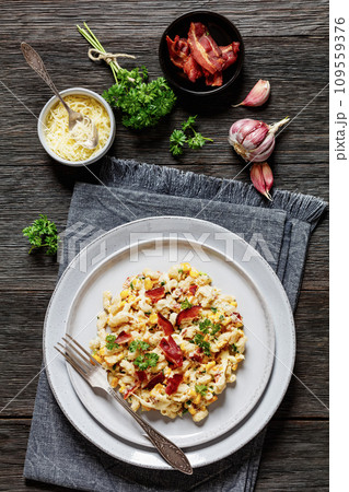 ortion of mac and cheese with corn, bacon topped with panko breadcrumbs on plate on dark wooden table 109559376