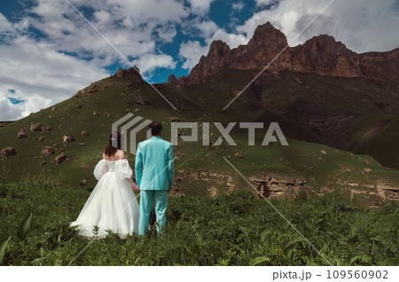 Wedding. A guy and a girl in a white dress stand on a green field opposite the mountains and look at the high rocky ridges 109560902