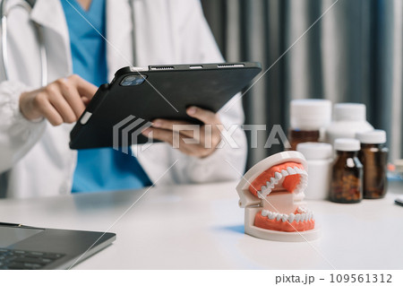 Doctor stomatologist is working on a Tablet computer and tooth model in a modern office in the morning at the desk. 109561312