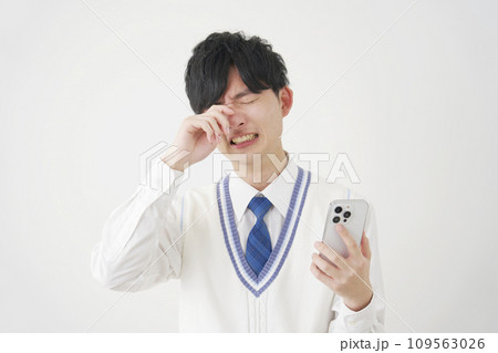 スマートフォンを持って泣く男子高校生 白背景 スマートフォンを持って泣く男子高校生 白背景 109563026