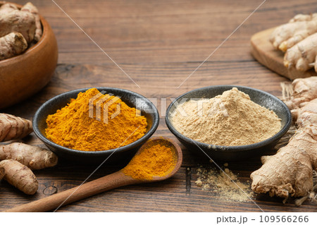 Bowls of ginger and curcuma ground to powder and whole ginger and turmeric roots on kitchen table. Aromatic spices. Bowls of ginger and curcuma ground to powder and whole ginger and turmeric roots on kitchen table. Aromatic spices. 109566266