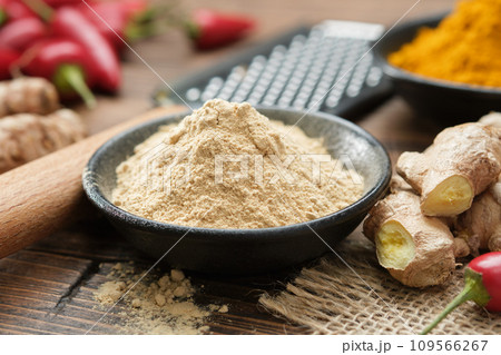 Bowl of ginger ground to powder and fresh whole ginger roots. Turmeric and red hot peppers on background. Aromatic spices. Ingredients for cooking and Ayurveda. 109566267