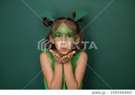 An attractive girl with a dragon scale pattern on her face, on a green studio background, sends an air kiss An attractive girl with a dragon scale pattern on her face, on a green studio background, sends an air kiss 109566860