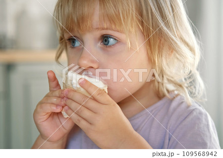 Baby girl enjoying ice cream. Pretty little toddler eating an ice-cream indoors, at home. Dining room background. Small child eats plombir and cream messy on her mouth. Cute kid with tasty sweet food. Baby girl enjoying ice cream. Pretty little toddler eating an ice-cream indoors, at home. Dining room background. Small child eats plombir and cream messy on her mouth. Cute kid with tasty sweet food. 109568942