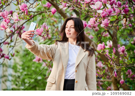 Beautiful woman taking selfie with smartphone among spring blossoms with soft focus on the background. Beautiful woman taking selfie with smartphone among spring blossoms with soft focus on the background. 109569082